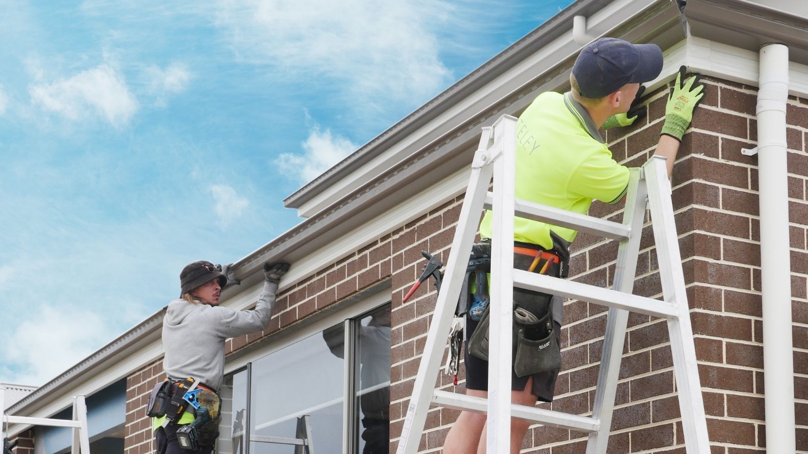 Two roofers installing gutters on a house